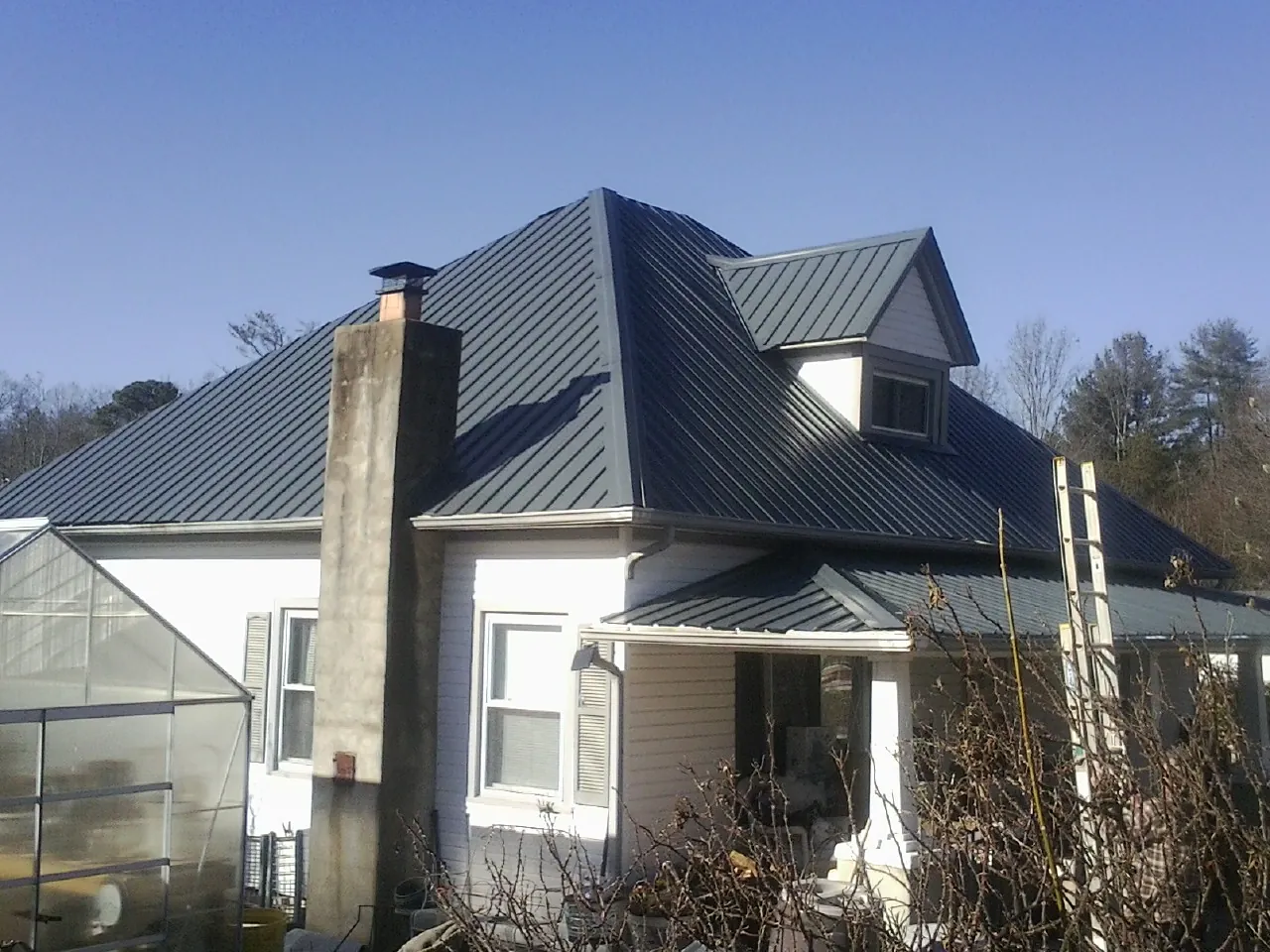 Dark blue standing seam metal roof on a white farmhouse with dormer — Slate & Tile Roof Repair by Roofing Brothers in Lamoni