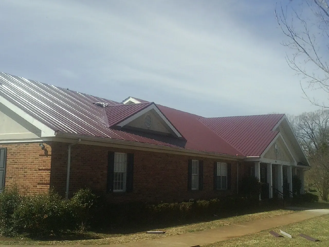 Red metal roof with gabled entries on a long brick building, from a Hail Damage Roof Repair job in Lamoni
