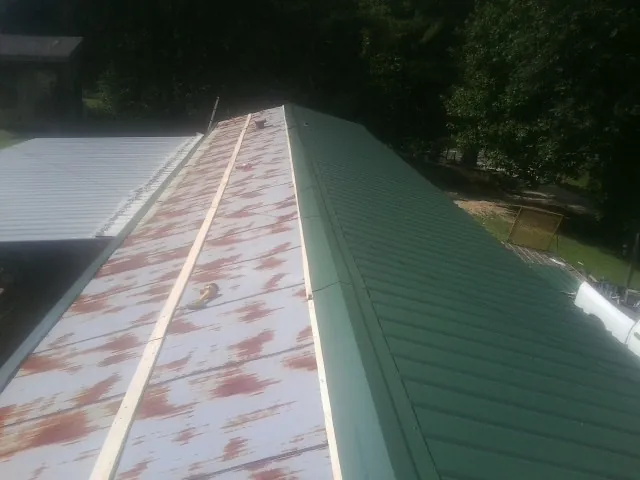 Old rusted panels beside newly installed green metal roofing — Wind Damage Roof Repair by Roofing Brothers in Lamoni