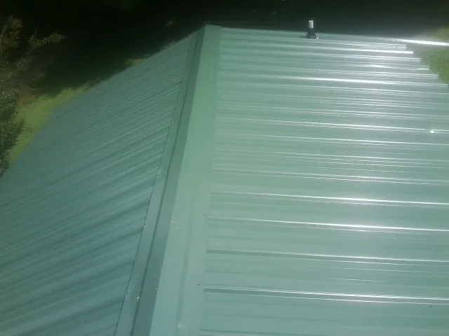 New green metal panels meeting at the ridge of a roof — Flat Roof Repair work by our crew in Lamoni