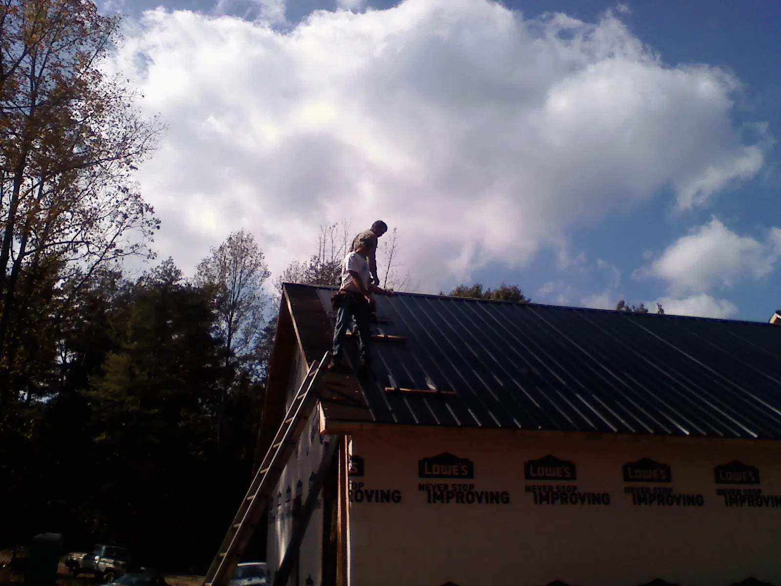 Roofer fastening dark metal panels high against a cloudy sky, from a Roof Inspection job in Lamoni