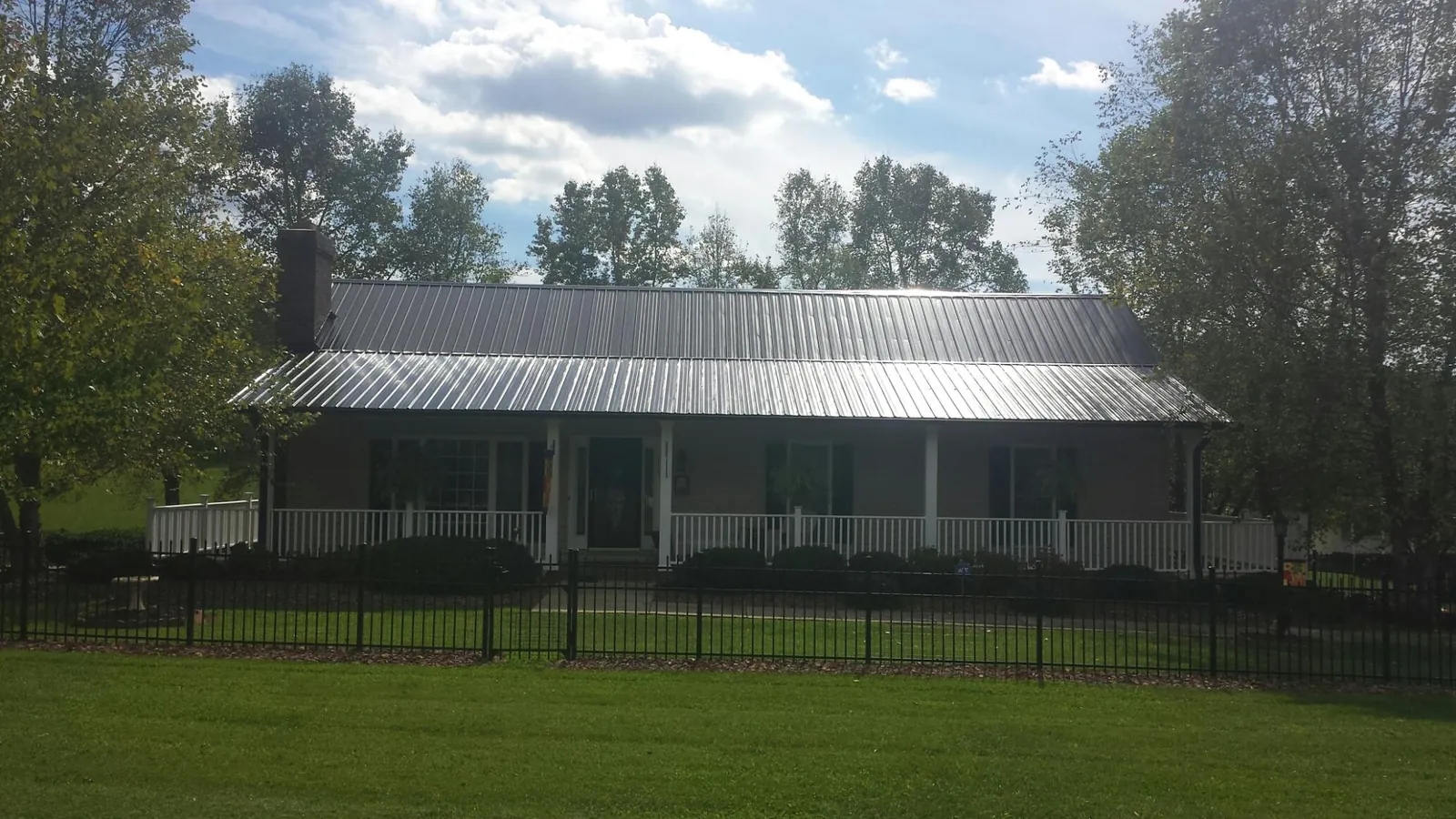 Gray metal roof on a brick ranch with a full width front porch — Gutter Guard Installation work by our crew in Lamoni