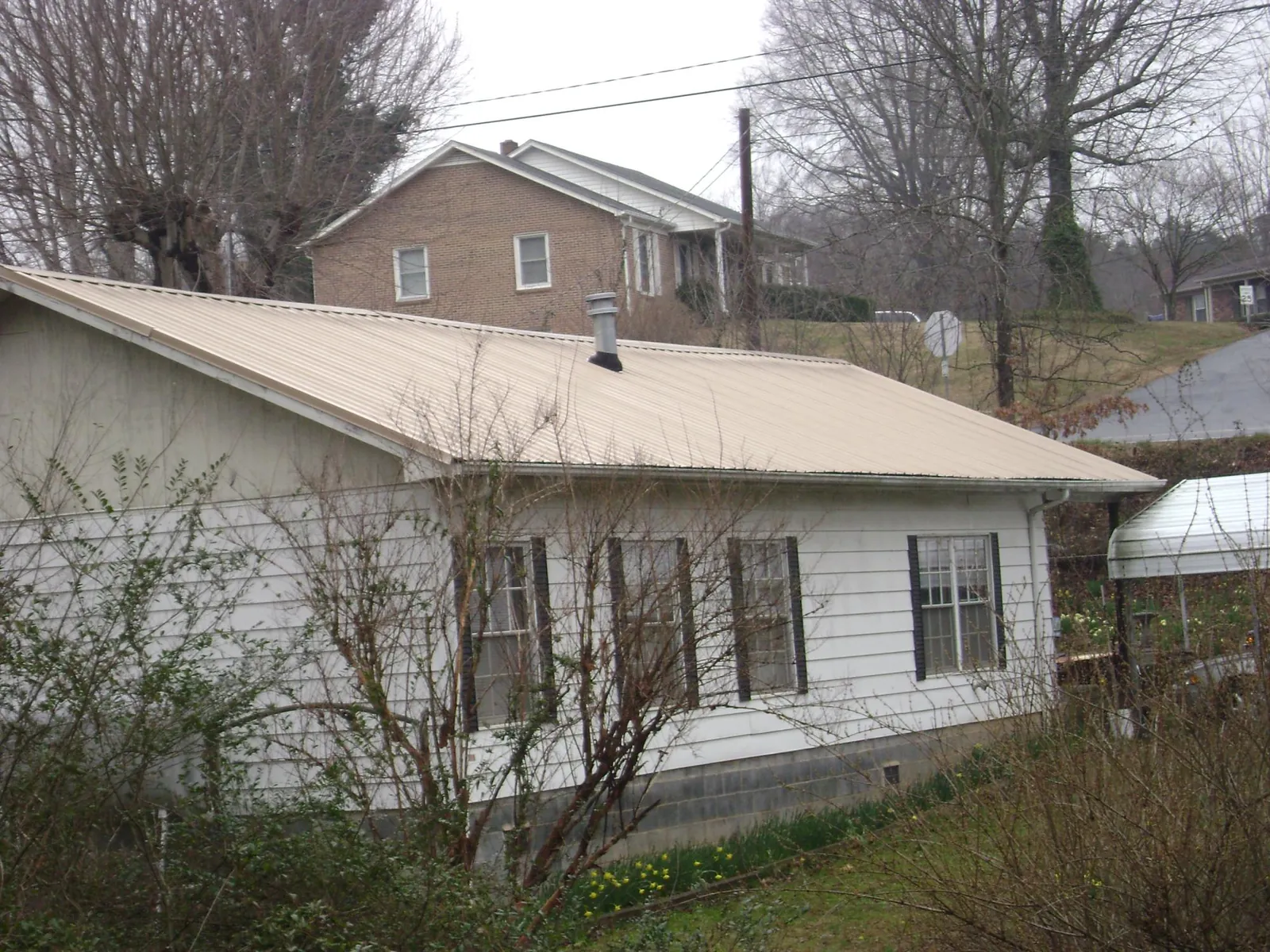 Tan metal roof on a white sided house set into a hillside — Commercial Roofing by Roofing Brothers in Lamoni
