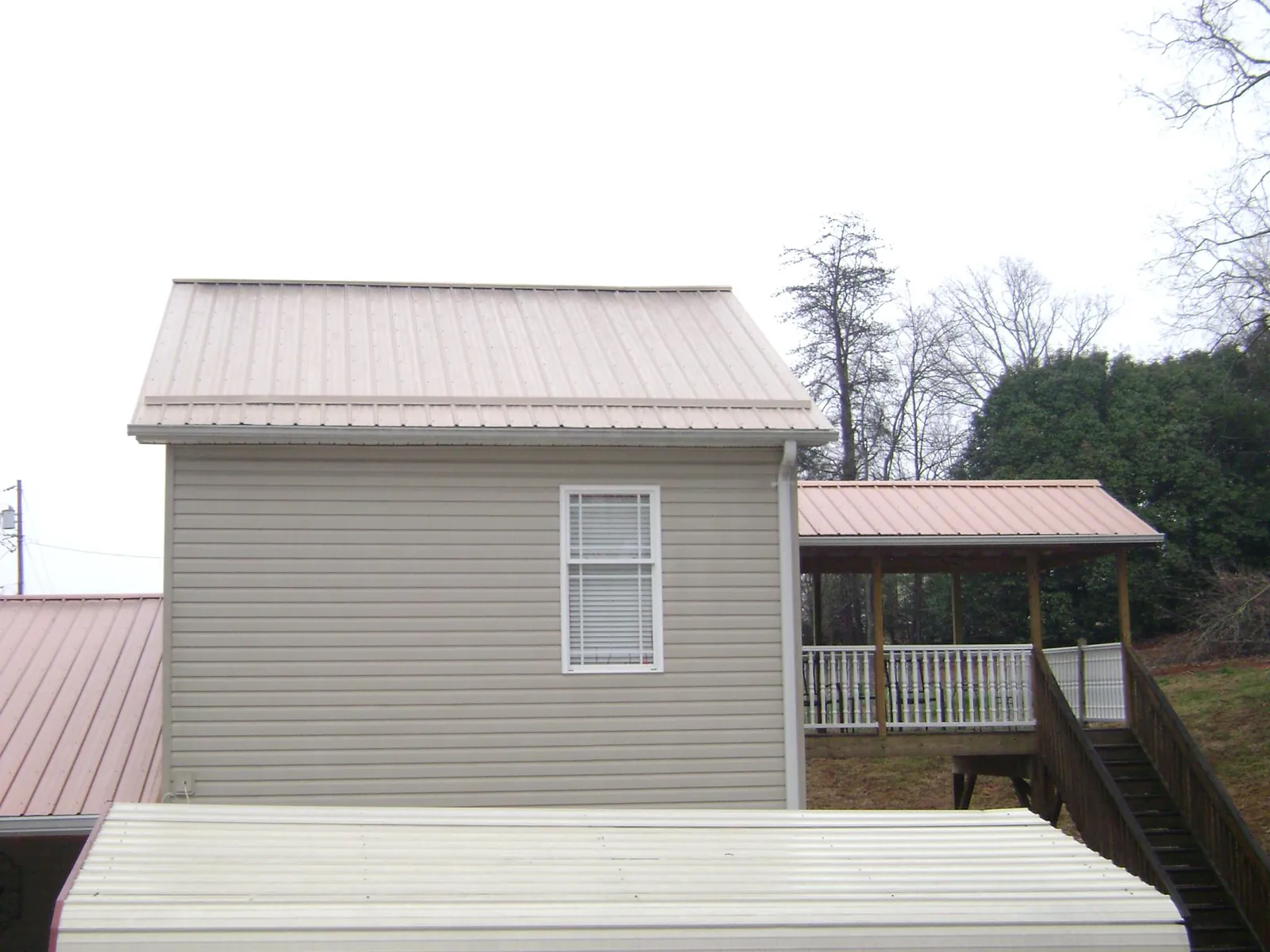 Tan metal roofs on a two story addition and attached porch, from a Roof Replacement job in Lamoni